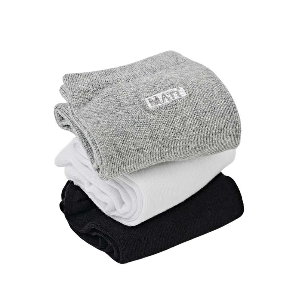 Product photography of three MAATI brand socks neatly stacked on a white background featuring a top grey sock with an embroidered white MAATI logo a middle white sock and a bottom black sock